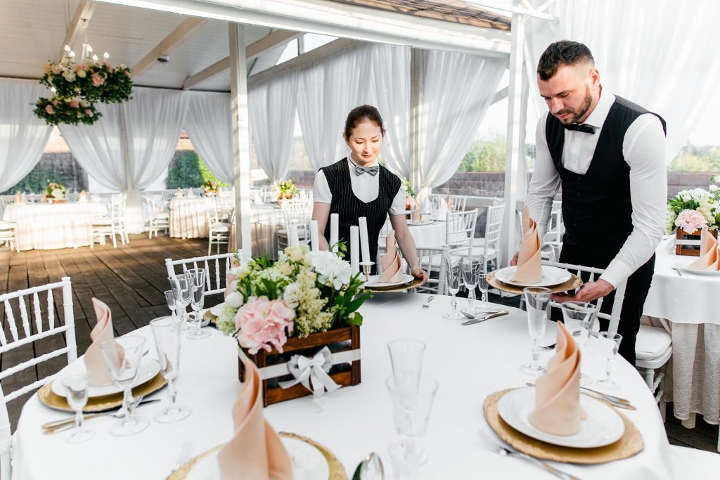 Two male and female IMESA_waiters serve tableware on the table in the restaurant